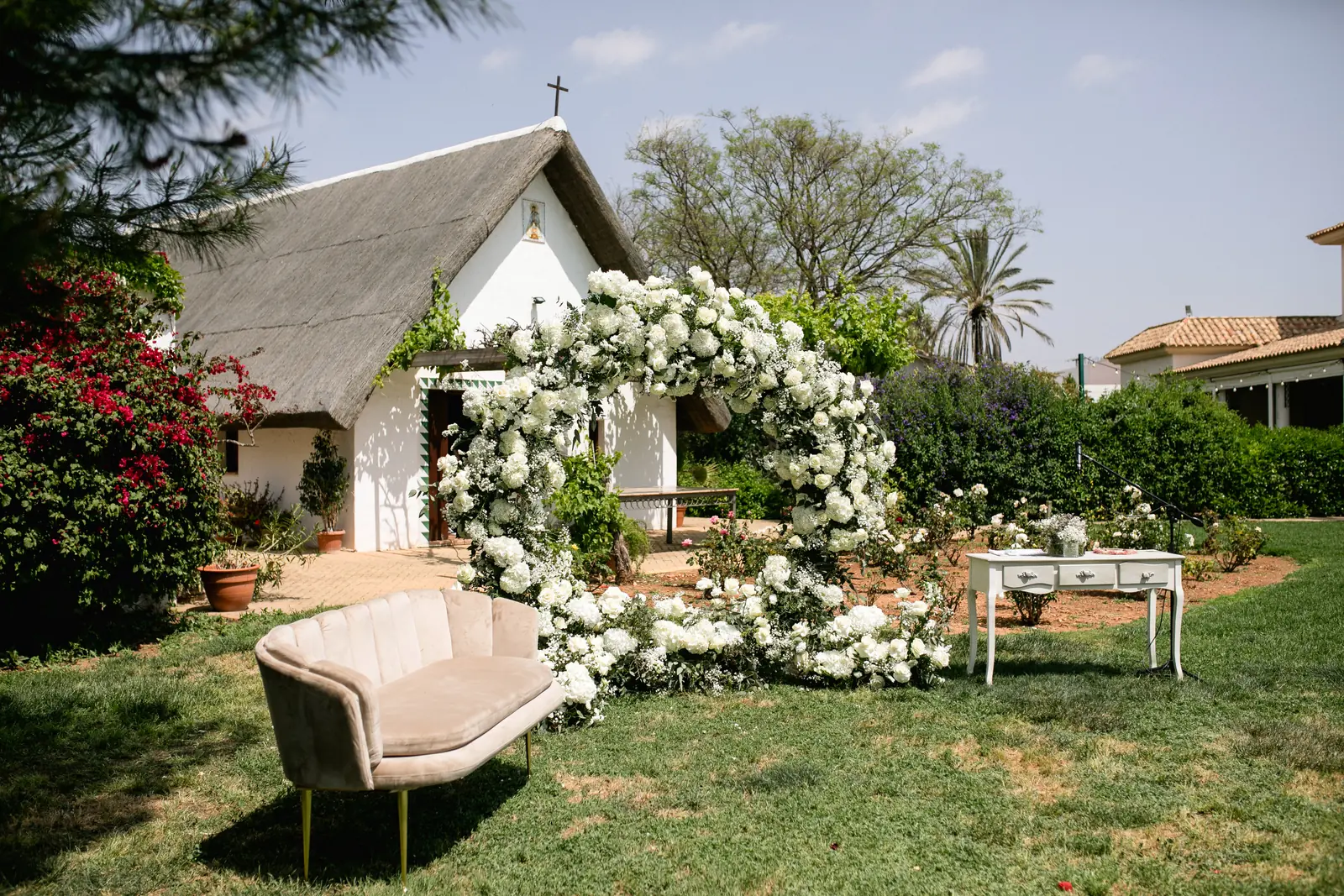 Arco de flores blancas y sofá vintage en un jardín preparado para una ceremonia